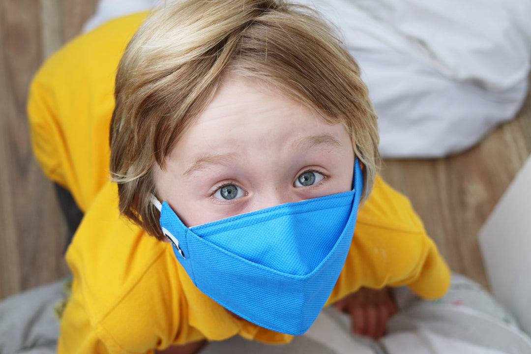 young boy looking up at the camera wearing a child size blue reusable face mask.