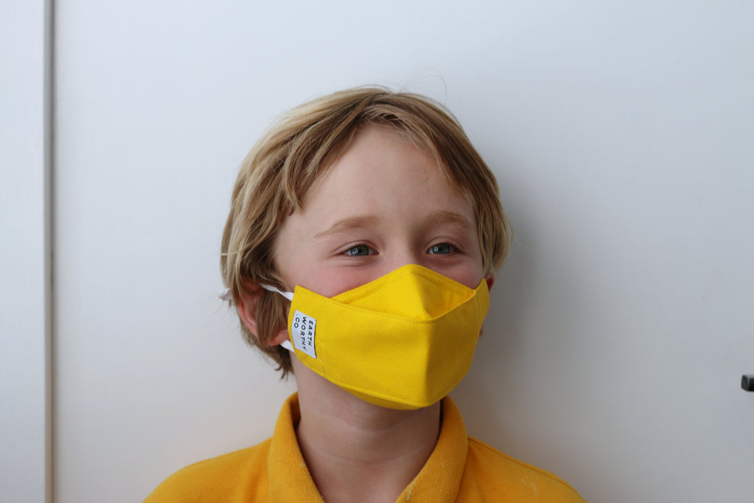 small boy in his school uniform wear a resuable children's face mask in yellow.